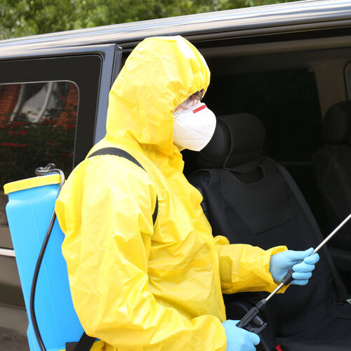 person in protective suit spraying a car's interior